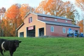 Light brown barn on a field surrounded by trees with orange leaves in the left side 